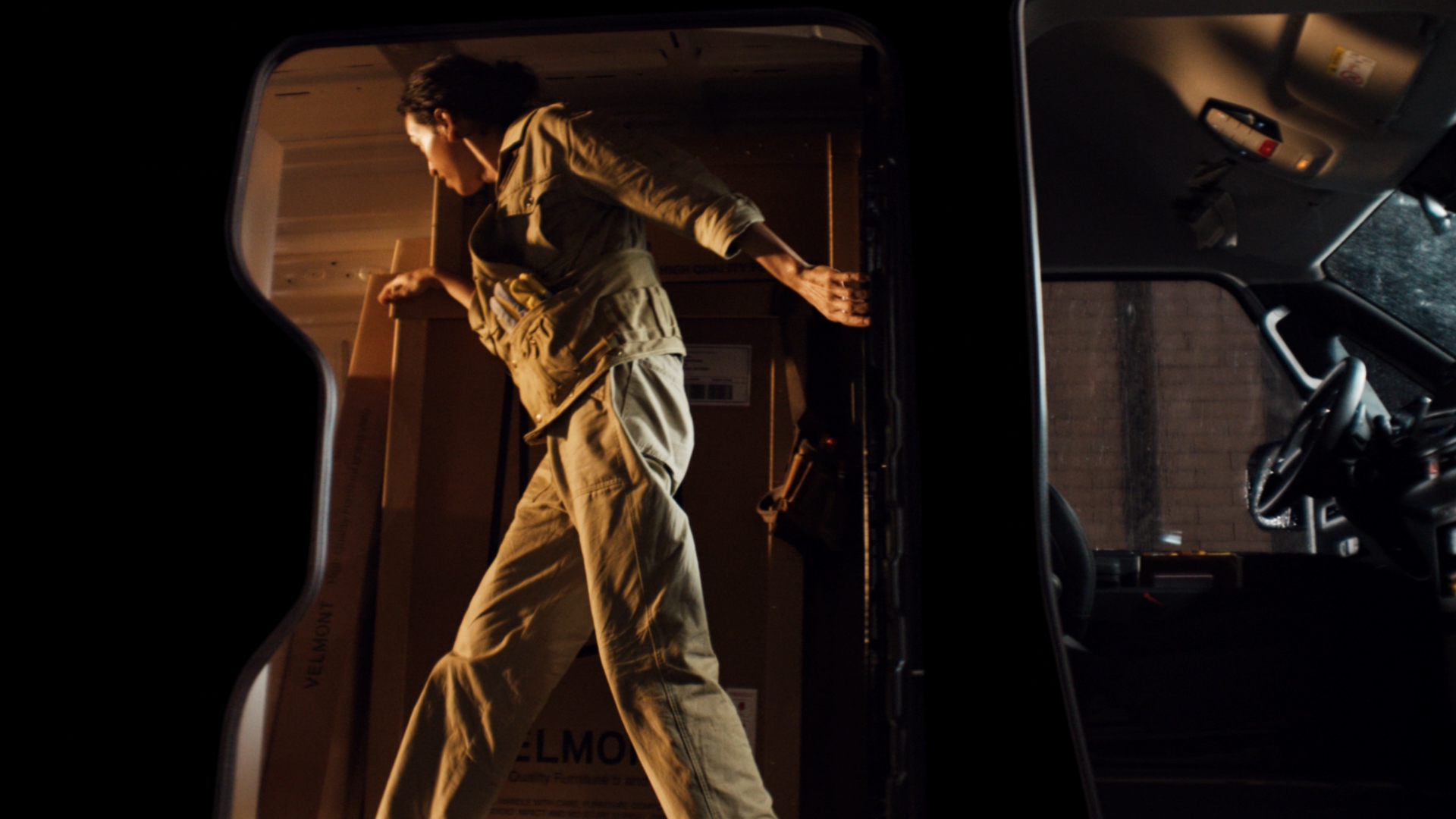 Worker standing upright inside the Kia PV5 Cargo High Roof cargo bay, arranging boxes