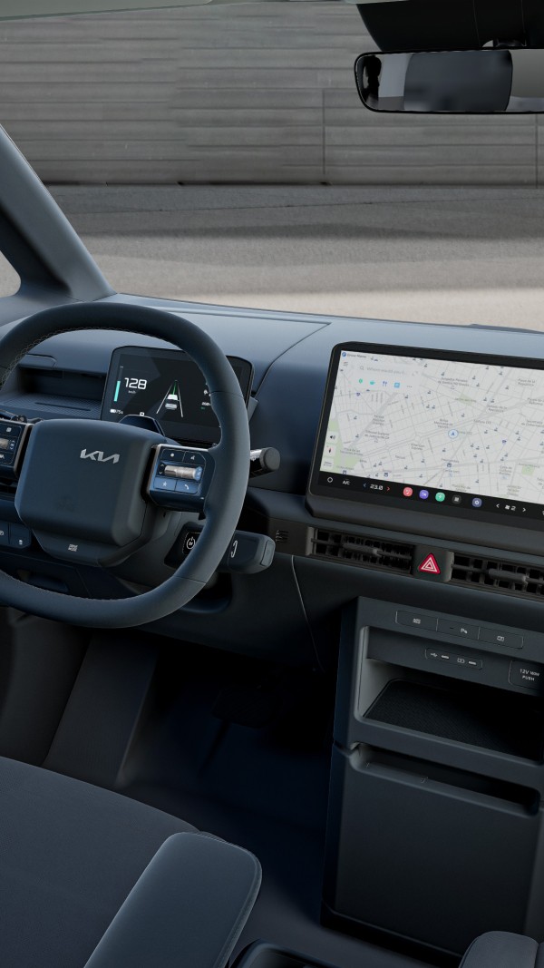 Angled interior view of the Kia PV5 cockpit showing the driver's seat, steering wheel and infotainment display